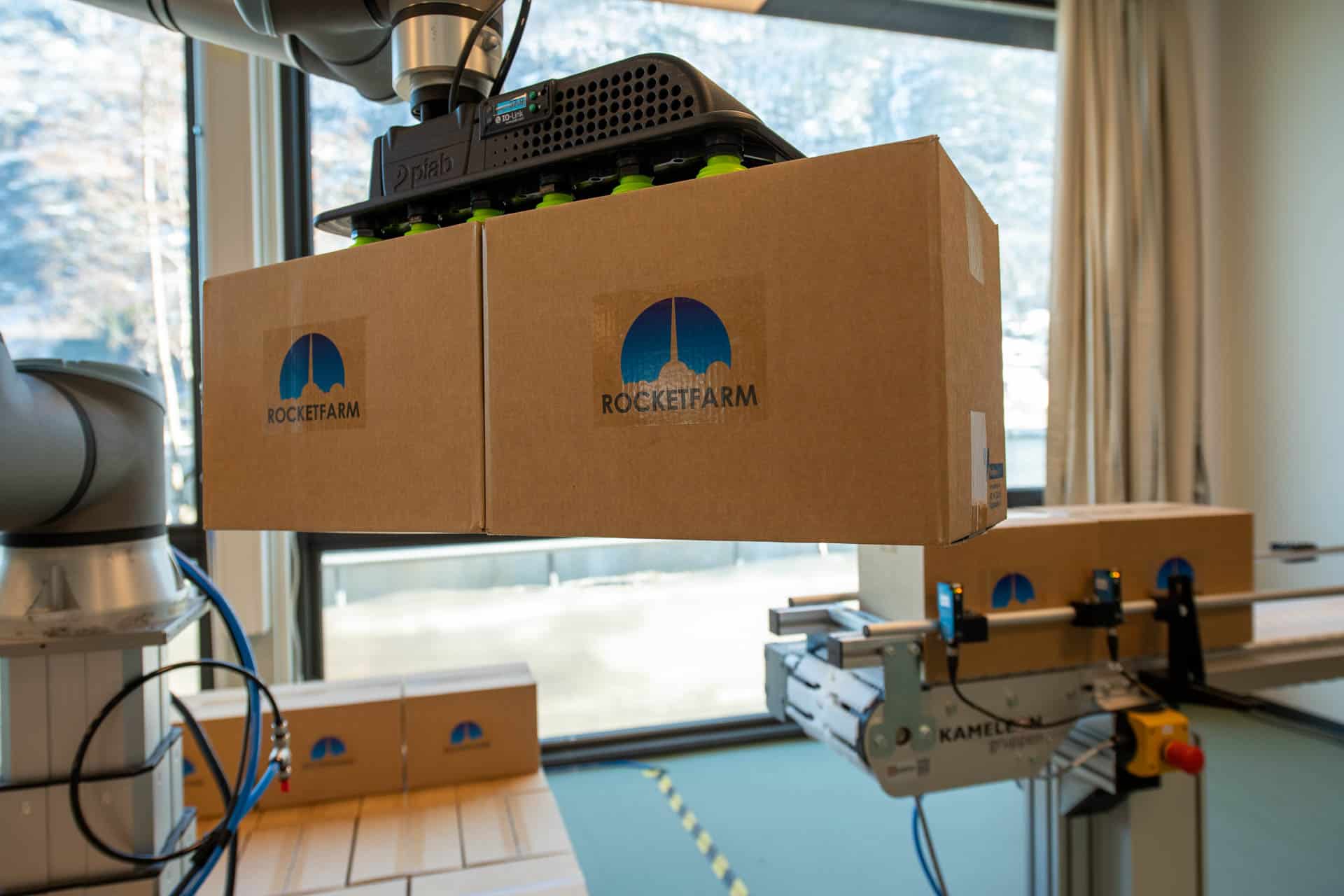 Piab gripper lifting two boxes with Rocketfarm logo on.